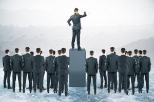 Businessman standing on pedestal and looking into the distance with other businesspeople around. Leadership concept
